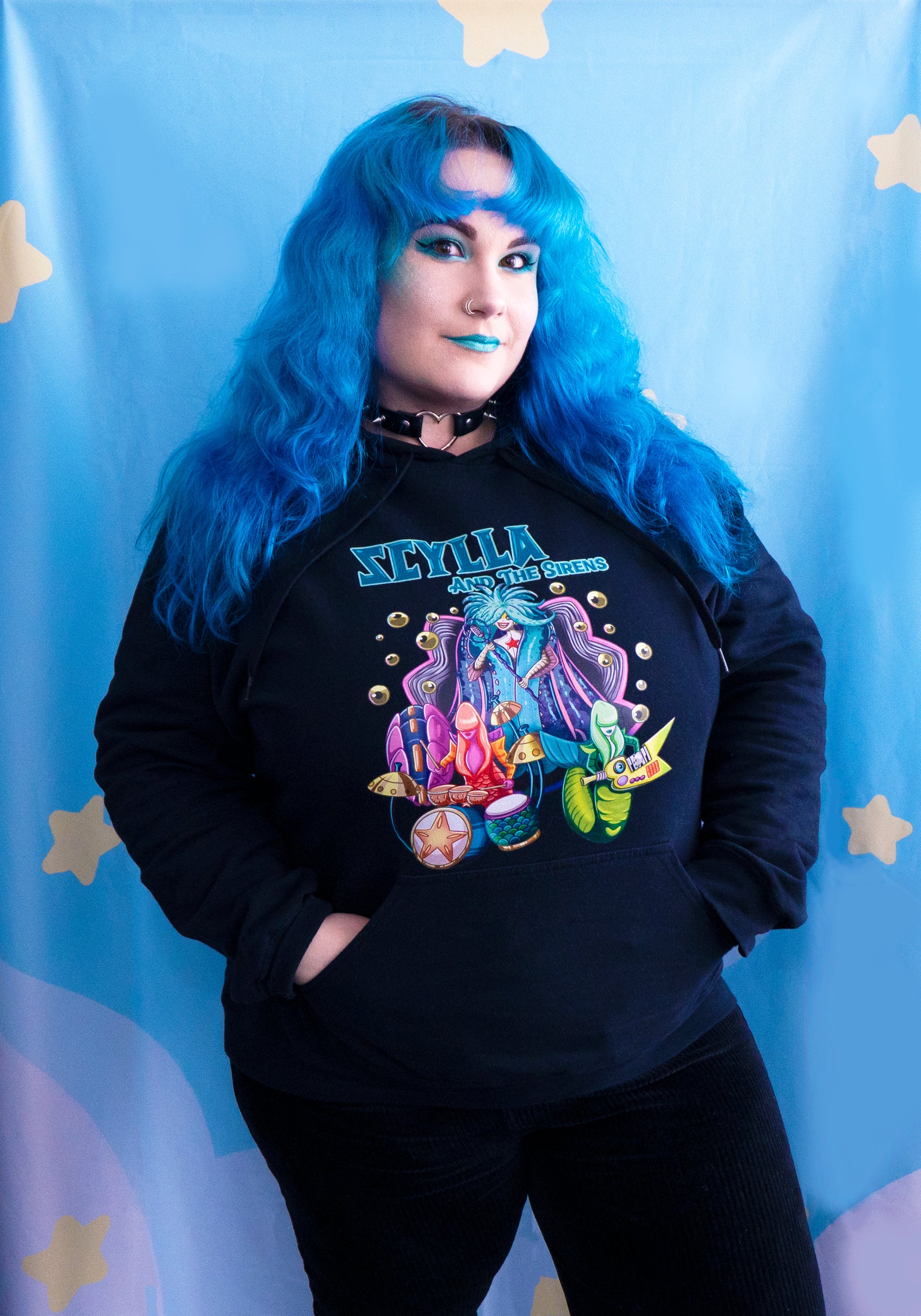 Person wearing a black hoodie with a colorful Scylla And The Sirents graphic design on a blue background with star shapes.