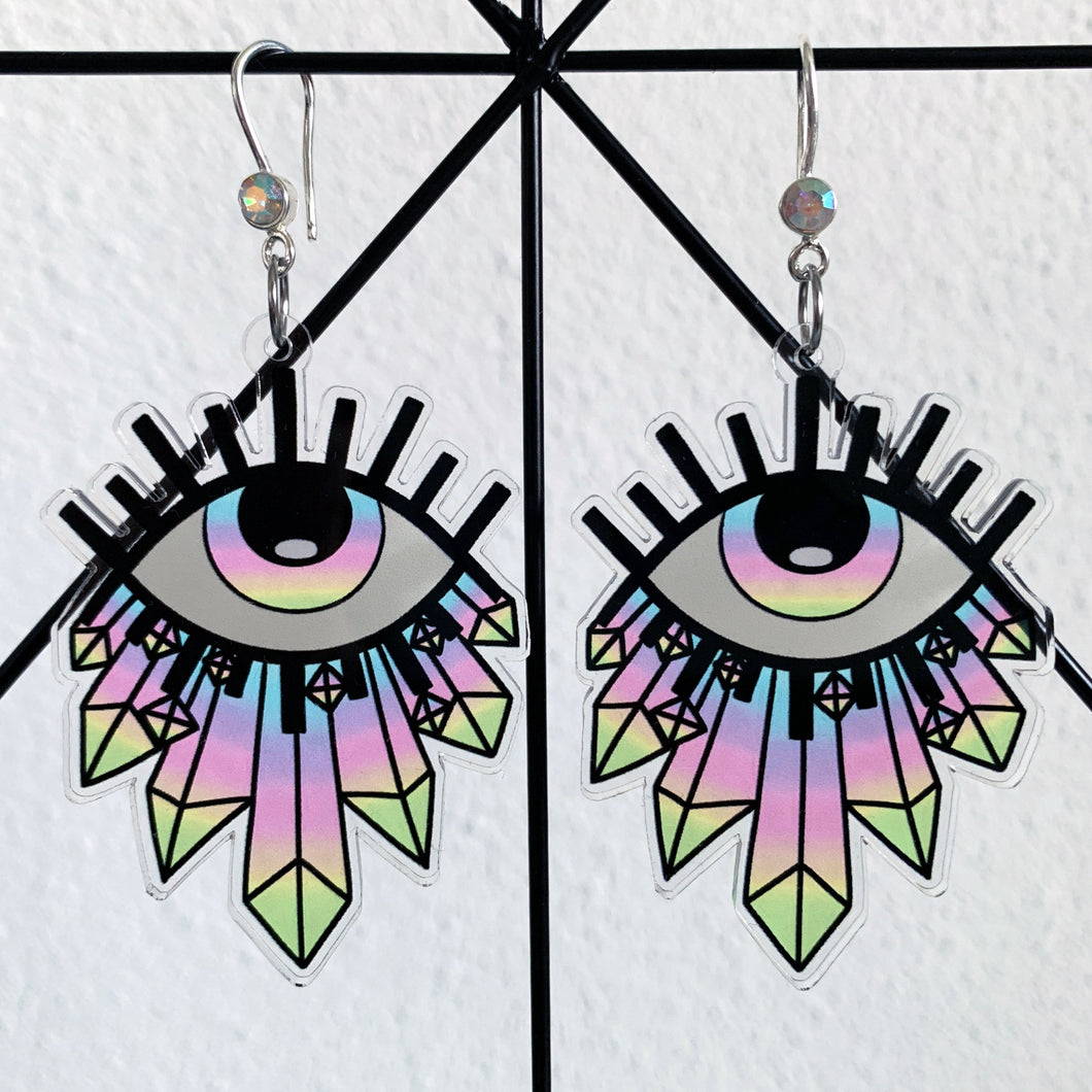 Large earrings featuring a stylized eye looking up, with blue, prurple, pink, yellow and green gradient see through iris and illustrated crystals at the bottom. With a silver hook with a multicolored rhinestone.